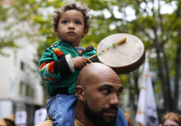 FILE - Khalako Lloyd, 2, of the Mandan and Hidatsa tribes, beats on a drum while carried on the shoulder of his father, Julius Lloyd during a celebratory march for Indigenous Peoples Day, Oct. 9, 2023, in Seattle. (AP Photo/Lindsey Wasson, File)