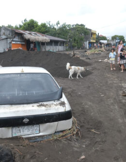 Residents stay beside a car partially buried by volcanic mud that had flowed down from Mayon volcano after heavy rains caused by Tropical Storm Trami hit Guinobatan town, Albay province, Philippines on Wednesday Oct. 23, 2024. (AP Photo/John Michael Magdasoc)