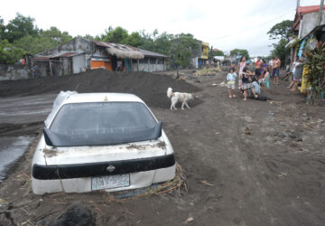 Residents stay beside a car partially buried by volcanic mud that had flowed down from Mayon volcano after heavy rains caused by Tropical Storm Trami hit Guinobatan town, Albay province, Philippines on Wednesday Oct. 23, 2024. (AP Photo/John Michael Magdasoc)