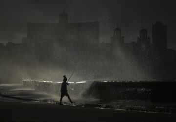 A person fishes along the boardwalk as waves crash during a power outage in Havana, Monday, Oct. 21, 2024. (AP Photo/Ramon Espinosa)