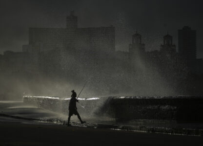 A person fishes along the boardwalk as waves crash during a power outage in Havana, Monday, Oct. 21, 2024. (AP Photo/Ramon Espinosa)