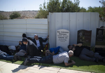 People take cover as a siren warns of incoming rockets during the funeral of Alexei Popov, who was killed during a rocket attack fired from Lebanon last weekend, at the Tel Regev cemetery in the outskirts of Haifa, northern Israel, Monday, Oct. 21, 2024. (AP Photo/Leo Correa)