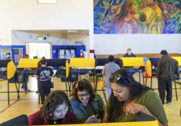 First-time voter Elizabeth Vazquez, 33, left, receives in-person assistance from her mother, Estela Gonzalez, middle, and Victoria Arriaga, as she casts her ballot at Barrio Action Youth & Family Center in the El Sereno area of Los Angeles on Tuesday, Nov. 5, 2024. (AP Photo/Damian Dovarganes)