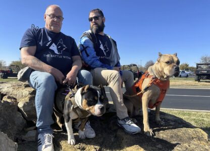 Retired Army First Sgt. Timothy Siebenmorgen, left, and retired Marine Corps Cpl. Mark Atkinson sit with their service dogs, Rosie and Lexi on Thursday, Nov. 7, 2024, in Kansas City, Kan., during a group training session. Both veterans are part of Dogs 4 Valor that helps retired veterans and first responders in the Kansas City area work with their service dogs to help manage depression, anxiety and other challenges. (AP Photo/Nick Ingram)