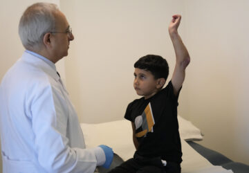 Orthopedic and spine surgeon Dr. Rachid Haidar, left, checks Adam Afana, 5, who was brought to Lebanon from Gaza for treatment after nearly losing his left arm in an Israeli airstrike that killed his father and sister, as his uncle, Eid Afana, right, stands next to him at the American University of Beirut Medical Center, in Beirut, Lebanon, Monday, July 15, 2024. (AP Photo/Hussein Malla)