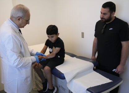 Orthopedic and spine surgeon Dr. Rachid Haidar, left, checks the arm of a Palestinian boy, Adam Afana, 5, who was brought to Lebanon from Gaza for treatment after nearly losing his left arm in an Israeli airstrike that killed his father and sister, at the American University of Beirut Medical Center, in Beirut, Lebanon, Monday, July 15, 2024. (AP Photo/Hussein Malla)