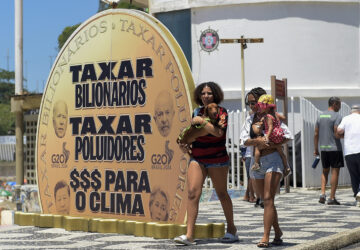 Women walk past a giant coin that reads in Portuguese 