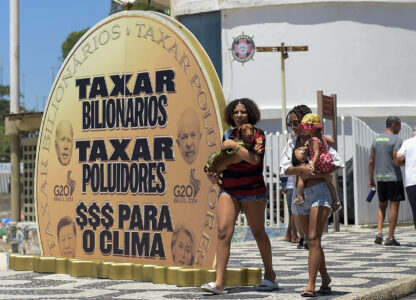 Women walk past a giant coin that reads in Portuguese 