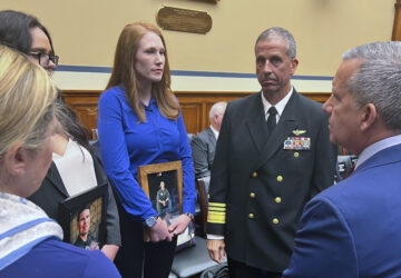 FILE - Amber Sax, center, holds a photo of her late husband, Marine Corps MV-22B pilot Capt. John Sax, as she and other family members who have lost service members to Osprey crashes talk with Vice Adm. Carl Chebi, Commander of U.S. Naval Air Systems Command, center right, and Peter Belk, acting Assistant Secretary of Defense for Readiness, right, before a hearing on the programs safety record, Wednesday, June 12, 2024, on Capitol Hill in Washington. (AP Photo/Tara Copp)