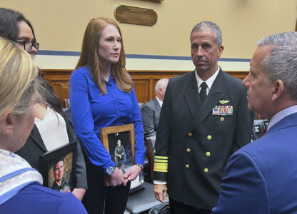 FILE - Amber Sax, center, holds a photo of her late husband, Marine Corps MV-22B pilot Capt. John Sax, as she and other family members who have lost service members to Osprey crashes talk with Vice Adm. Carl Chebi, Commander of U.S. Naval Air Systems Command, center right, and Peter Belk, acting Assistant Secretary of Defense for Readiness, right, before a hearing on the programs safety record, Wednesday, June 12, 2024, on Capitol Hill in Washington. (AP Photo/Tara Copp)