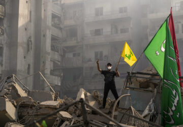 FILE - A man flashes the victory sign as he holds up a Hezbollah flag while standing on the ruins of his apartment after an Israeli airstrike in Dahiyeh, Beirut, Lebanon, on Nov. 1, 2024. (AP Photo/Hassan Ammar, File)