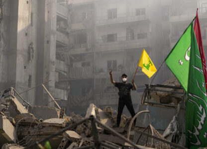 FILE - A man flashes the victory sign as he holds up a Hezbollah flag while standing on the ruins of his apartment after an Israeli airstrike in Dahiyeh, Beirut, Lebanon, on Nov. 1, 2024. (AP Photo/Hassan Ammar, File)