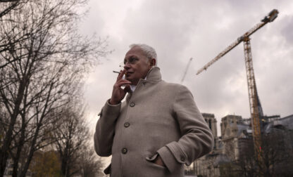 Notre-Dame de Paris cathedral chief architect Philippe Villeneuve smokes a cigarette by the cathedral during an interview with Associated Press, Tuesday, Dec. 3, 2024 in Paris. (AP Photo/Louise Delmotte)