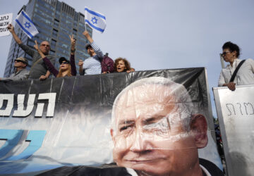 Supporters of Israel's Prime Minster Benjamin Netanyahu, seen in poster, gather outside a court in Tel Aviv, Israel, Tuesday, Dec. 10, 2024 as Netanyahu is set to take the stand in his long-running trial on corruption charges. (AP Photo/Ariel Schalit)