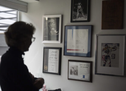 Two-time Olympian Joan Wilder looks at memorabilia at her home on Nov. 22, 2024, in Bend, Ore., including an image of her competing at bottom right. (AP Photo/Jenny Kane)