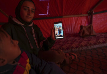 Sitting next to her son Wael, left, Reem Ajour shows a picture of her daughter, Masaa, and her husband, Talal, on her cellphone in a camp outside Zuweida, Gaza Strip, Nov. 20, 2024. (AP Photo/Abdel Kareem Hana)