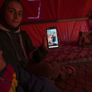 Sitting next to her son Wael, left, Reem Ajour shows a picture of her daughter, Masaa, and her husband, Talal, on her cellphone in a camp outside Zuweida, Gaza Strip, Nov. 20, 2024. (AP Photo/Abdel Kareem Hana)