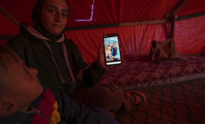 Sitting next to her son Wael, left, Reem Ajour shows a picture of her daughter, Masaa, and her husband, Talal, on her cellphone in a camp outside Zuweida, Gaza Strip, Nov. 20, 2024. (AP Photo/Abdel Kareem Hana)