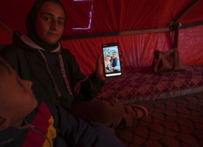 Sitting next to her son Wael, left, Reem Ajour shows a picture of her daughter, Masaa, and her husband, Talal, on her cellphone in a camp outside Zuweida, Gaza Strip, Nov. 20, 2024. (AP Photo/Abdel Kareem Hana)