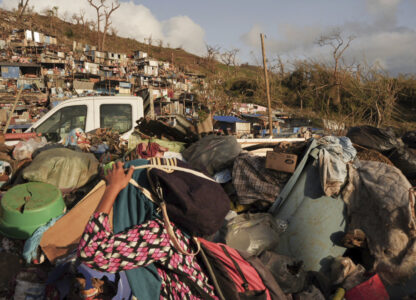 A woman carrying her belongings walks past debris after Cyclone Chido in the Kaweni slum Thursday, Dec. 19, 2024, on the outskirts of Mamoudzou, in the French Indian Ocean island of Mayotte. (AP Photo/Adrienne Surprenant)