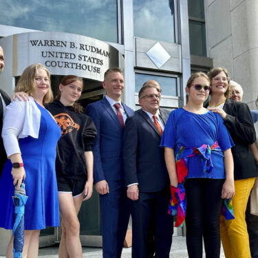 FILE - Two teens challenging New Hampshire's new law banning transgender girls from girls' sports teams pose with their families and attorneys in Concord, N.H., Monday, Aug. 19, 2024, after a judge granted an emergency request to allow one of the girls to play soccer while their lawsuit continues. (AP Photo/Holly Ramer, File)