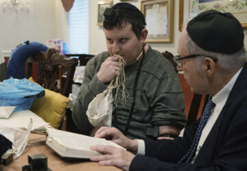 Dov Marcus, left, kisses the knotted fringes -- known as tzitzit – of his prayer shawl after wrapping the leather straps of tefillin and praying with his uncle, Chaim Orlan, in Teaneck, N.J., on Friday, Dec. 20, 2024. (AP Photo/Luis Andres Henao)