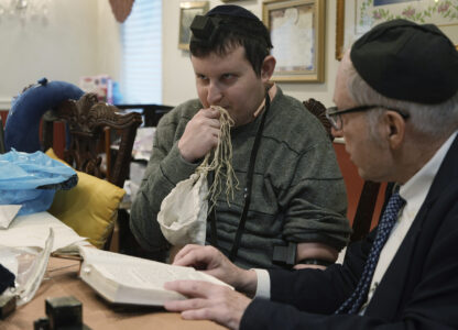 Dov Marcus, left, kisses the knotted fringes -- known as tzitzit – of his prayer shawl after wrapping the leather straps of tefillin and praying with his uncle, Chaim Orlan, in Teaneck, N.J., on Friday, Dec. 20, 2024. (AP Photo/Luis Andres Henao)