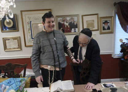 Dov Marcus smiles after wrapping the leather straps of tefillin to pray with his uncle, Chaim Orlan, in Teaneck, N.J., on Friday, Dec. 20, 2024. (AP Photo/Luis Andres Henao)