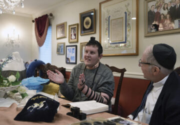 Dov Marcus, left, sings with his mother, Debbie Marcus, after wrapping the leather straps of tefillin and praying with his uncle, Chaim Orlan, right, in Teaneck, N.J., on Friday, Dec. 20, 2024. (AP Photo/Luis Andres Henao)