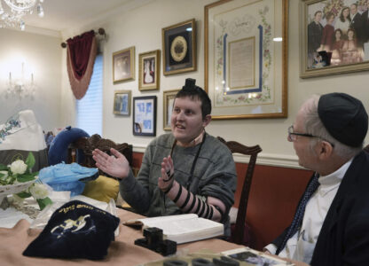 Dov Marcus, left, sings with his mother, Debbie Marcus, after wrapping the leather straps of tefillin and praying with his uncle, Chaim Orlan, right, in Teaneck, N.J., on Friday, Dec. 20, 2024. (AP Photo/Luis Andres Henao)