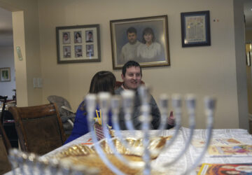 Dov Marcus talks to his mother, Debbie Marcus, at their dining table near the branched candelabra called a menorah, in Teaneck, N.J., on Friday, Dec. 20, 2024. (AP Photo/Luis Andres Henao)