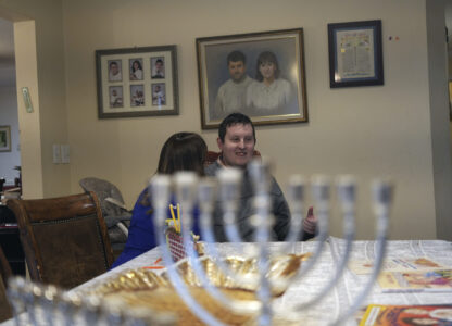 Dov Marcus talks to his mother, Debbie Marcus, at their dining table near the branched candelabra called a menorah, in Teaneck, N.J., on Friday, Dec. 20, 2024. (AP Photo/Luis Andres Henao)