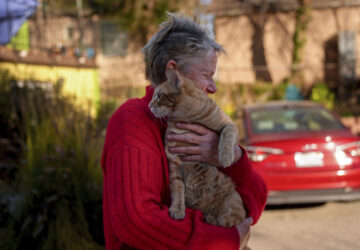 Denise Johnson, whose home is one of the few that survived the Eaton Fire in her neighborhood in Altadena, Calif., holds her cat Ramsey as she and her two children hunker down without power to care for their pets and protect the home Tuesday, Jan. 14, 2025. (AP Photo/Jae C. Hong)