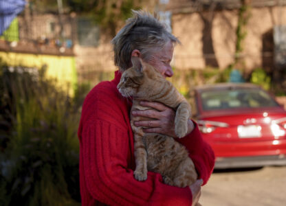 Denise Johnson, whose home is one of the few that survived the Eaton Fire in her neighborhood in Altadena, Calif., holds her cat Ramsey as she and her two children hunker down without power to care for their pets and protect the home Tuesday, Jan. 14, 2025. (AP Photo/Jae C. Hong)