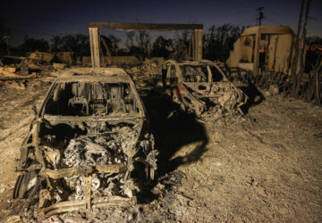 Charred vehicles are illuminated by utility lights at homes destroyed by the Palisades Fire in the Pacific Palisades neighborhood of Los Angeles, Thursday, Jan. 16, 2025. (AP Photo/Damian Dovarganes)