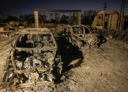 Charred vehicles are illuminated by utility lights at homes destroyed by the Palisades Fire in the Pacific Palisades neighborhood of Los Angeles, Thursday, Jan. 16, 2025. (AP Photo/Damian Dovarganes)