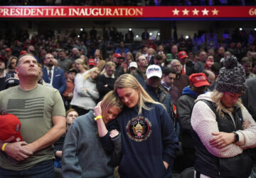 Supporters of President Donald Trump bow their heads during the invocation while watching inauguration ceremonies taking place at the U.S. Capitol on screens at Capitol One Arena in Washington, Monday, Jan. 20, 2025. (AP Photo/Mark Schiefelbein)