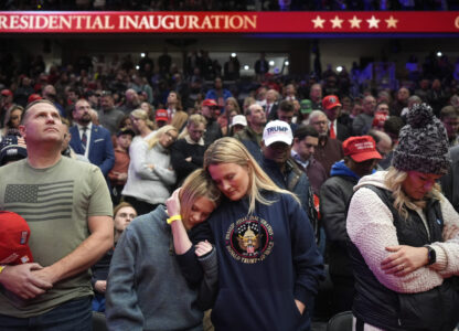 Supporters of President Donald Trump bow their heads during the invocation while watching inauguration ceremonies taking place at the U.S. Capitol on screens at Capitol One Arena in Washington, Monday, Jan. 20, 2025. (AP Photo/Mark Schiefelbein)