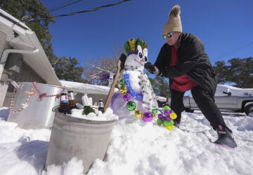 Stacy Centanni refreshes her Mardi Gras festooned snowman as it melts, the day after a record-setting snowstorm in River Ridge, La., a suburb of New Orleans, Wednesday, Jan. 22, 2025. (AP Photo/Gerald Herbert)