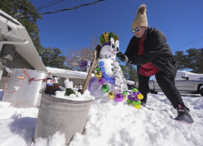 Stacy Centanni refreshes her Mardi Gras festooned snowman as it melts, the day after a record-setting snowstorm in River Ridge, La., a suburb of New Orleans, Wednesday, Jan. 22, 2025. (AP Photo/Gerald Herbert)