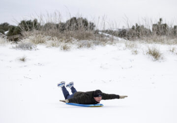 Alex Spiotta, from the Isle of Palms, S.C., uses a boogie board to sled across the beach after a winter storm dropped ice and snow Wednesday, Jan. 22, 2025, on the Isle of Palms, S.C. (AP Photo/Mic Smith)