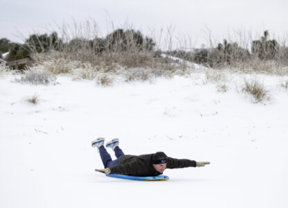 Alex Spiotta, from the Isle of Palms, S.C., uses a boogie board to sled across the beach after a winter storm dropped ice and snow Wednesday, Jan. 22, 2025, on the Isle of Palms, S.C. (AP Photo/Mic Smith)