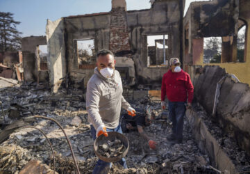 Homeowner David Marquez, left, holds a metal detector as he shows recovered metal items found with his father, Juan Pablo Alvarado, right, inside the walls of their multi-generational home in the aftermath of the Eaton Fire, Sunday, Jan. 19, 2025, in Altadena, Calif. (AP Photo/Damian Dovarganes)