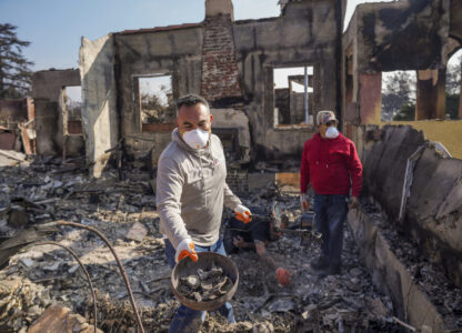 Homeowner David Marquez, left, holds a metal detector as he shows recovered metal items found with his father, Juan Pablo Alvarado, right, inside the walls of their multi-generational home in the aftermath of the Eaton Fire, Sunday, Jan. 19, 2025, in Altadena, Calif. (AP Photo/Damian Dovarganes)