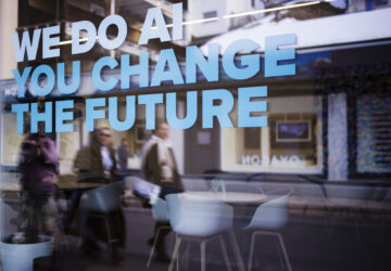 People reflected in a window with a slogan about AI at a representation of a company ahead of the World Economy Forum in Davos, Switzerland, Sunday, Jan. 19, 2025. (AP Photo/Markus Schreiber)