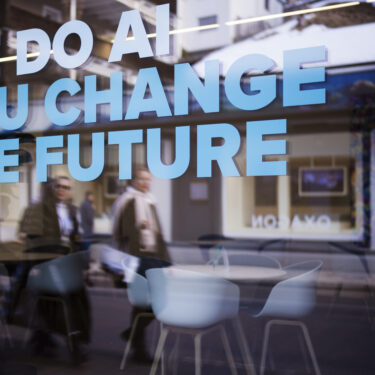 People reflected in a window with a slogan about AI at a representation of a company ahead of the World Economy Forum in Davos, Switzerland, Sunday, Jan. 19, 2025. (AP Photo/Markus Schreiber)