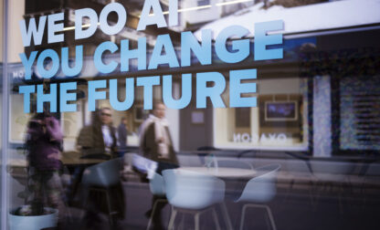 People reflected in a window with a slogan about AI at a representation of a company ahead of the World Economy Forum in Davos, Switzerland, Sunday, Jan. 19, 2025. (AP Photo/Markus Schreiber)