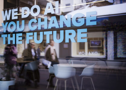 People reflected in a window with a slogan about AI at a representation of a company ahead of the World Economy Forum in Davos, Switzerland, Sunday, Jan. 19, 2025. (AP Photo/Markus Schreiber)