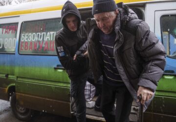 A volunteer of east SOS NGO helps en elderly man to walks out from a bus after evacuation from the frontline at a center for displaced people in Pavlohrad, Ukraine, Saturday, Feb. 1, 2024. (AP Photo/Evgeniy Maloletka)