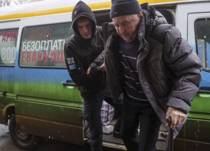 A volunteer of east SOS NGO helps en elderly man to walks out from a bus after evacuation from the frontline at a center for displaced people in Pavlohrad, Ukraine, Saturday, Feb. 1, 2024. (AP Photo/Evgeniy Maloletka)